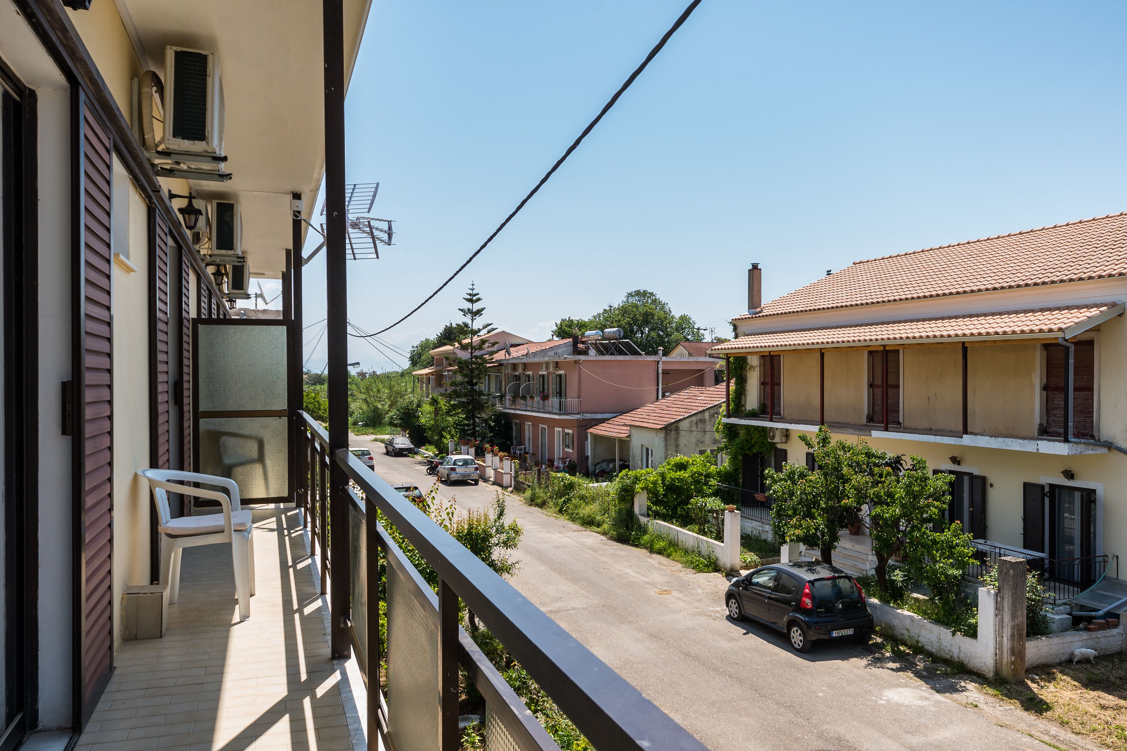 Une rue résidentielle bordée de maisons, un balcon avec une chaise et une voiture garée le long de la rue.