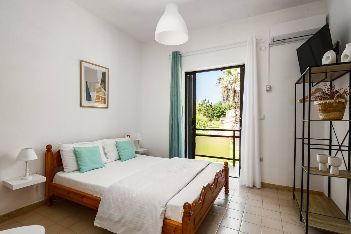 Quarto com cama de madeira, mesa de cabeceira, prateleira na parede e janela com cortinas.