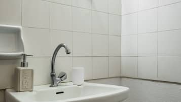 A bathroom with a white sink, a glass shelf, a toilet paper dispenser, and a plastic stool.