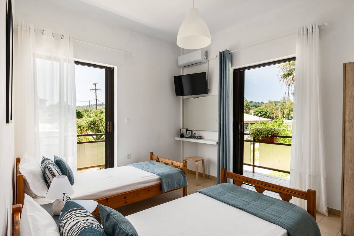 Quarto com duas camas, televisão e varanda com vista para o verde.
