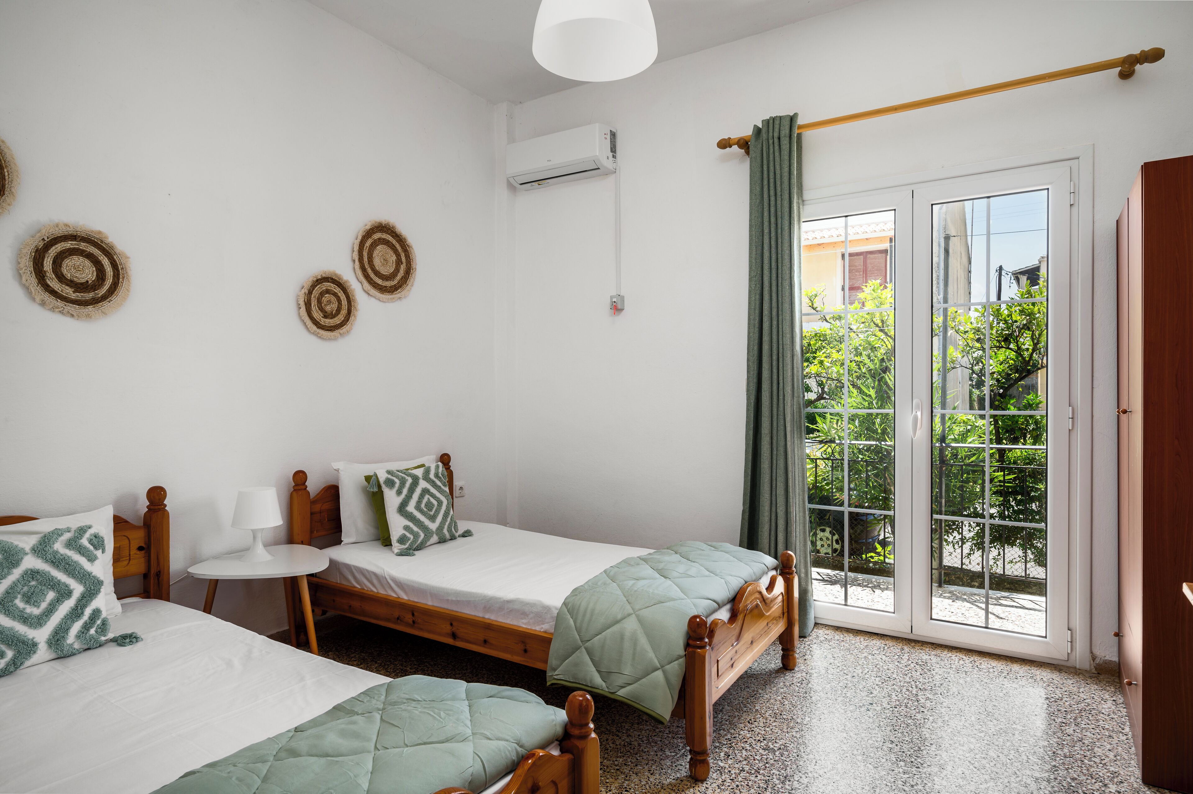 A room with two beds, a small table, a wall-mounted air conditioner, and a sliding glass door to a balcony.