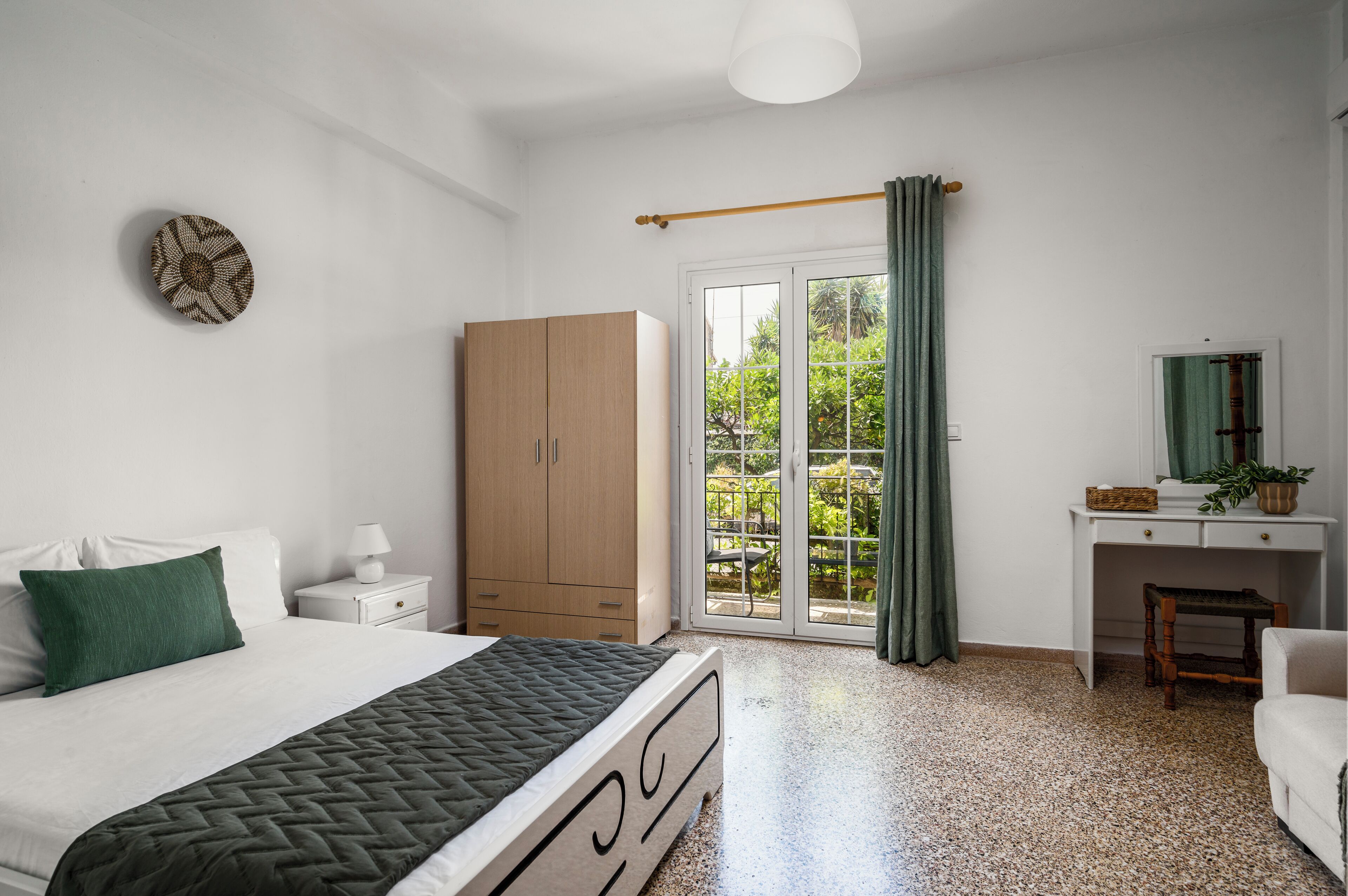 A bedroom with a bed, a wardrobe, a desk, and a view through a glass door.