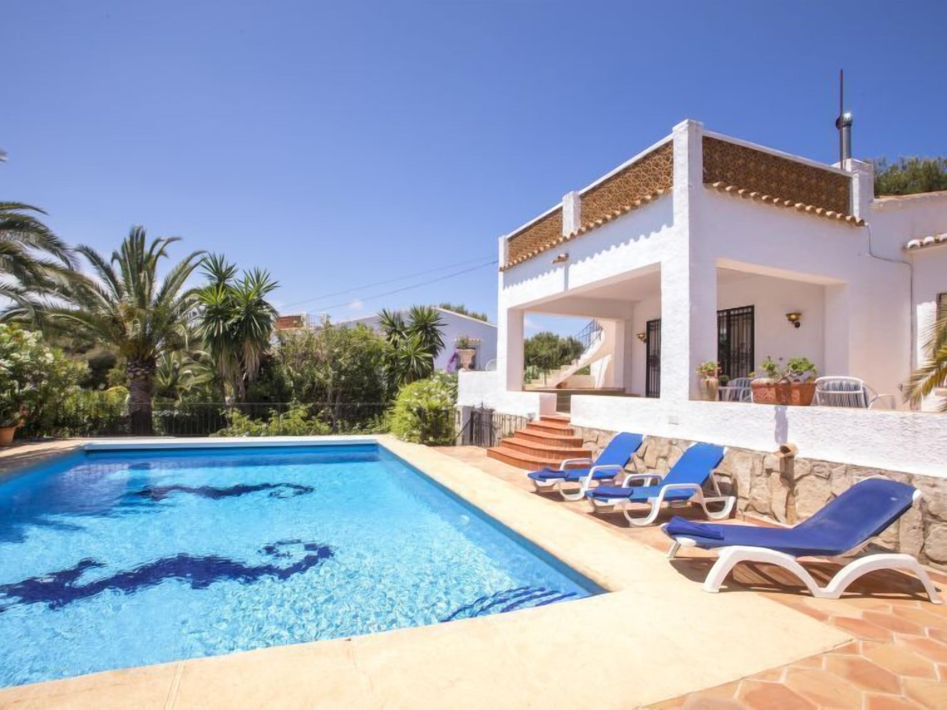 Un espace aménagé au bord de la piscine, avec une piscine à l’eau d’un bleu limpide, des murs blancs et des chaises longues bleues.