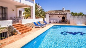 Área à beira da piscina com piscina azul cristalina, paredes brancas e teto em azulejos.