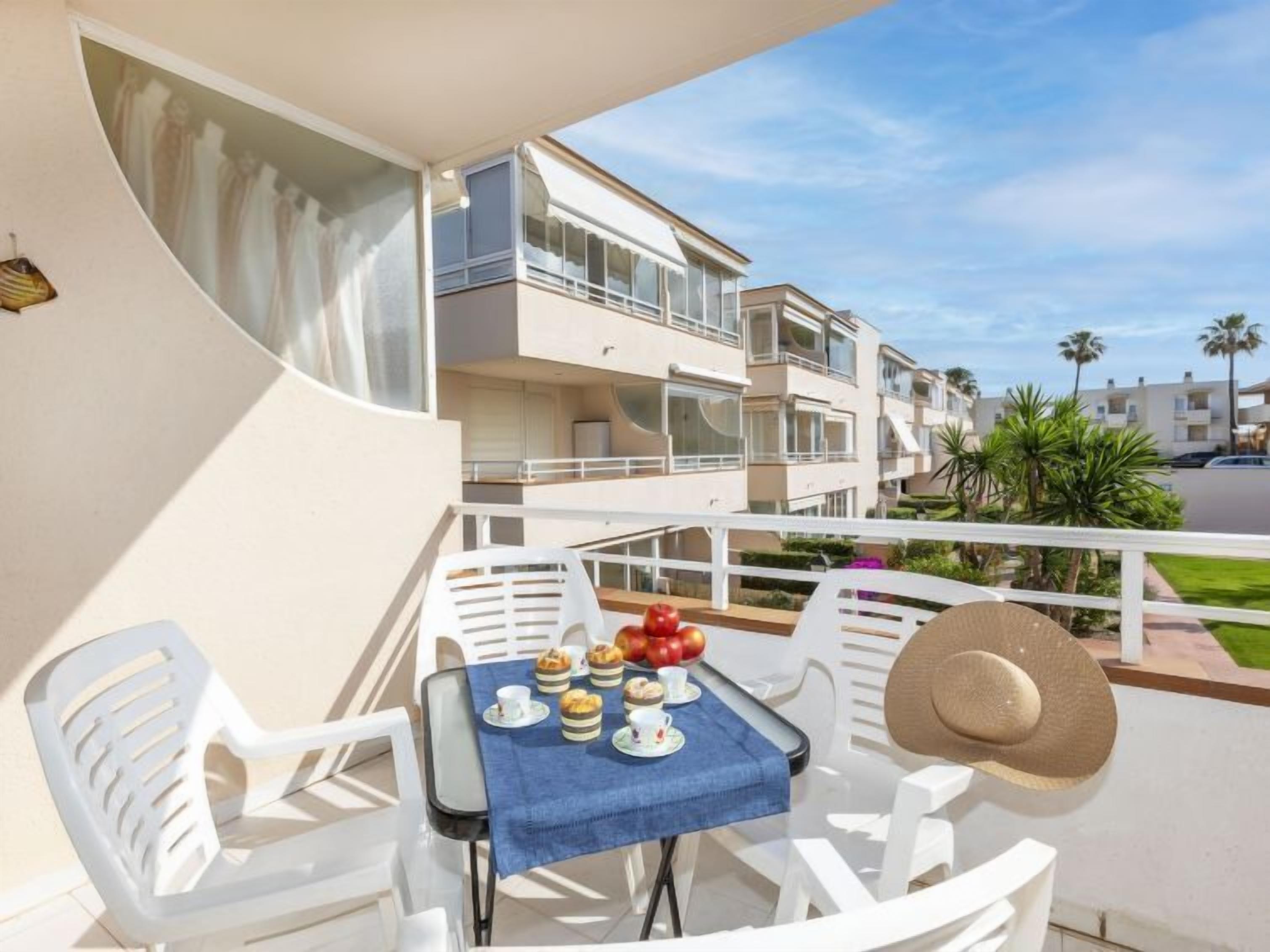 Een balkon met een ontbijttafel, witte stoelen en uitzicht op omliggende gebouwen.