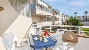A balcony with a table set for breakfast, white chairs, and a view of adjacent buildings. - Cala Gabriel by Interhome (Vinarós)
