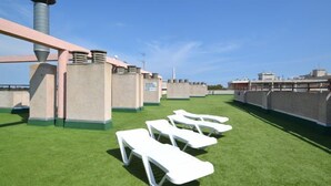 Eine Dachterrasse mit Kunstgrasanlage, weißen Lounge-Sesseln und einem großen Schornstein.