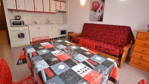 Ein gemütlicher Wohnbereich mit einer Küchenzeile, einem Sofa, einem Esstisch mit Tagesdecke und einer Holzkombination.