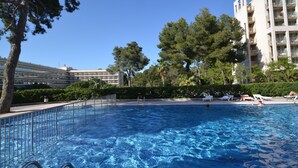Ein Schwimmbad mit klarem, blauem Wasser, umgeben von Bäumen und einem mehrstöckigen Gebäude im Hintergrund.