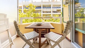 Un balcón con una mesa y dos sillas, vista de un edificio con balcones, y una ventana con persianas.