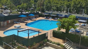 Piscina con tumbonas y sombrillas, rodeada de vegetación y edificios.