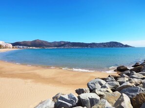 Ein Strand mit klarem, blauem Wasser, sandigem Ufer und Felsformationen.