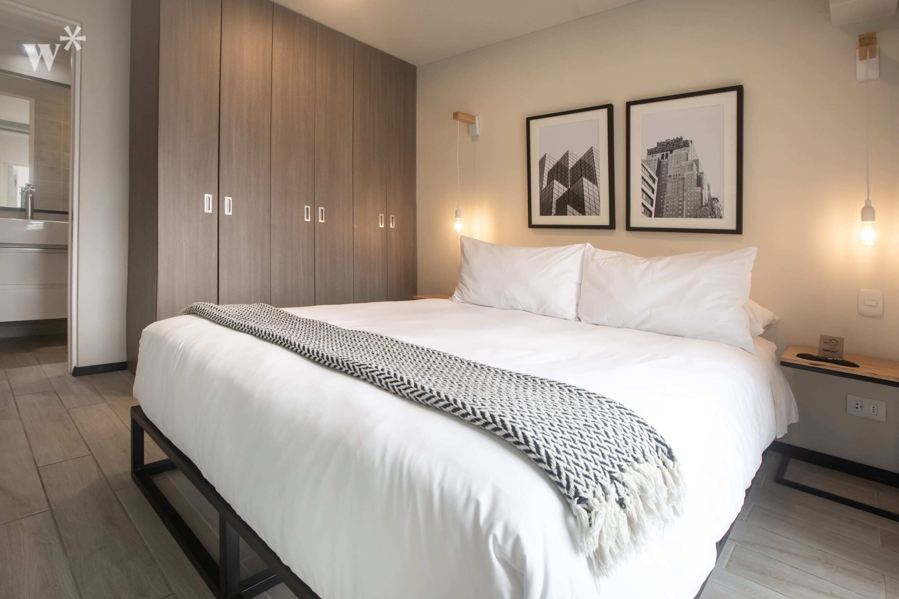 A modern bedroom with a large bed, wooden wardrobe, and two framed pictures on the wall.