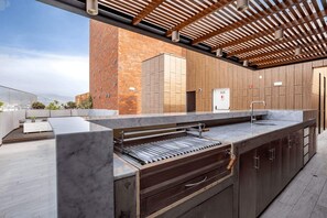 Eine Außenküche mit Grill, Holdekor und einer Pergola darüber.