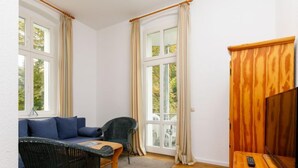 A cozy room with a sofa, two chairs, a wooden TV stand, and large windows with curtains. - App.11 Zinnowitzer Hof by Interhome (Zinnowitz)