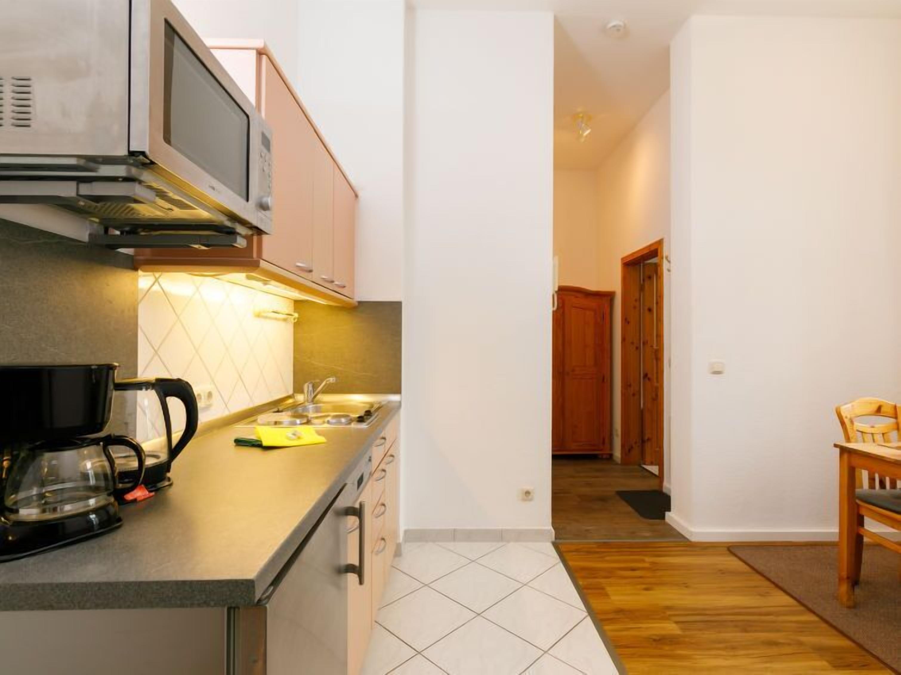 Cocina compacta con microondas, hervidor y una pequeña zona de comedor con una silla y mesa.