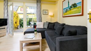 Een moderne woonkamer met een grijze bank, een houten salontafel en een televisie op een kast. Aan de muur hangt een landschapsschilderij, en er is een raam met gordijnen.