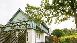 Een huis met een groen dak en witte muren, een houten omheining en een boom in de voortuin.
