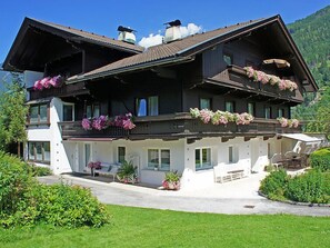 A two-story chalet with balconies adorned with flowers, a covered outdoor seating area, and a mountain backdrop. - Appartements Binderhof by Interhome (Aschau im Zillertal)