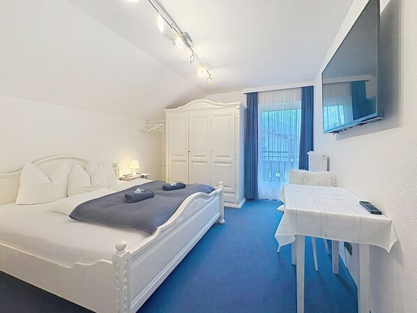 A hotel room with a bed, a bedside table, a TV, a wardrobe, and a balcony with curtains.