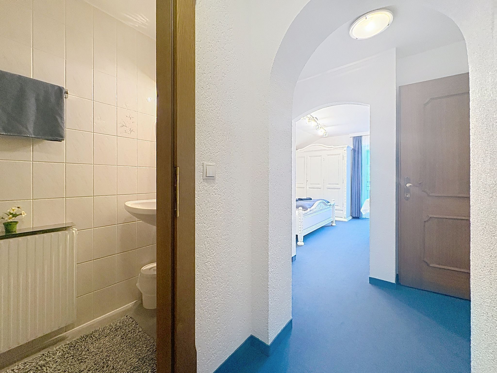 Ein Flur, der zu einem Schlafzimmer mit Bett, einem Badezimmer mit Waschbecken und Toilette sowie einer Tür führt.