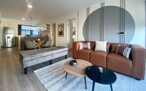 A modern living room with a brown leather sofa, a grey bench, and a round wooden coffee table. - Wynwood Grimaldo del Solar (Lima)