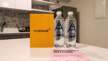 A hotel room with a yellow card labeled "Wywood House" and two water bottles with the "A" logo. A pink welcome card is also visible.