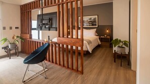 Una habitación de hotel moderna con un separador de madera, una cama, un escritorio y dos plantas en macetas.