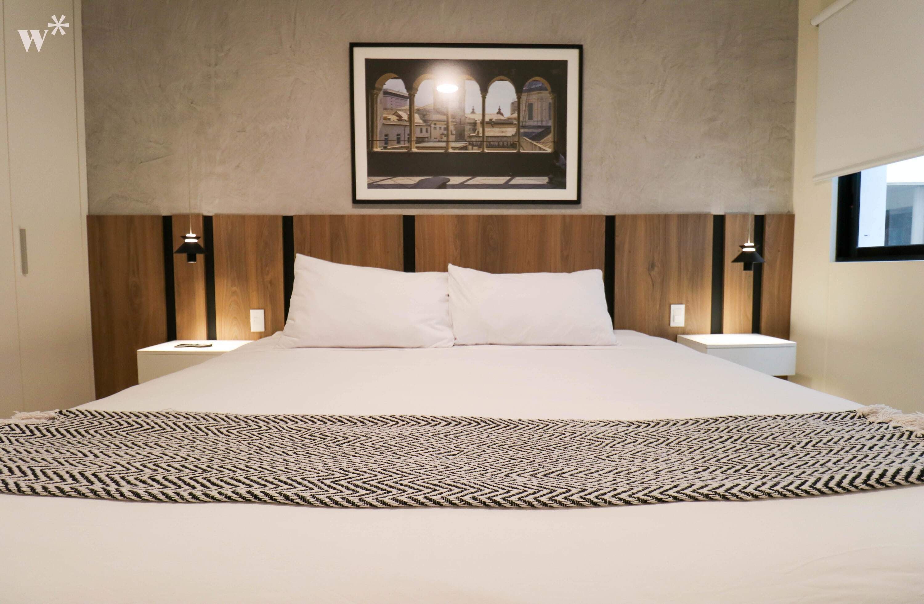 Un dormitorio con una cama grande, cabecera de madera, dos mesitas de noche con lámparas y un cuadro en la pared.
