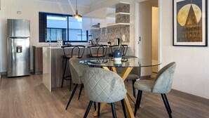 Una cocina moderna con una isla integrada, refrigerador de acero inoxidable y un comedor con mesa de vidrio y sillas acolchadas.