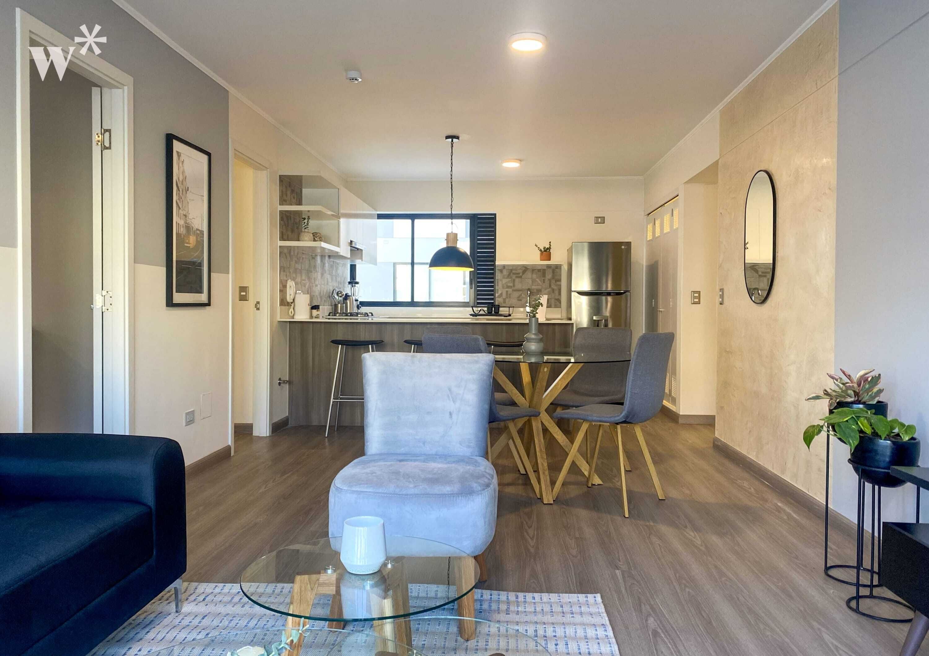 Una sala de estar moderna con una mesa de centro de vidrio, un sofá y un comedor con candelabro.