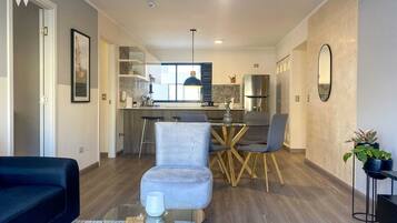 Una sala de estar moderna con una mesa de centro de vidrio, un sofá y un comedor con candelabro.