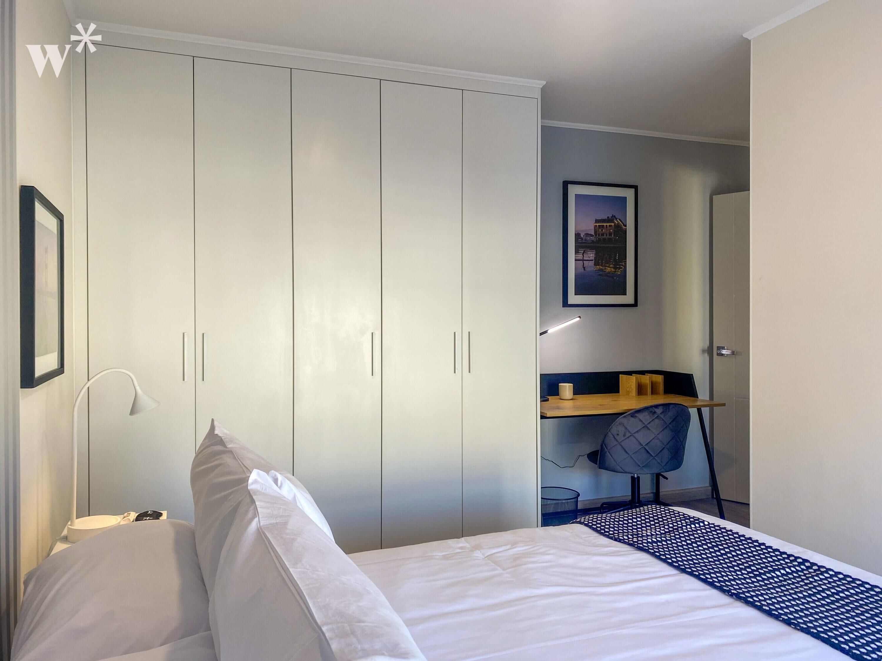A bedroom with a bed, a desk, and a wardrobe.