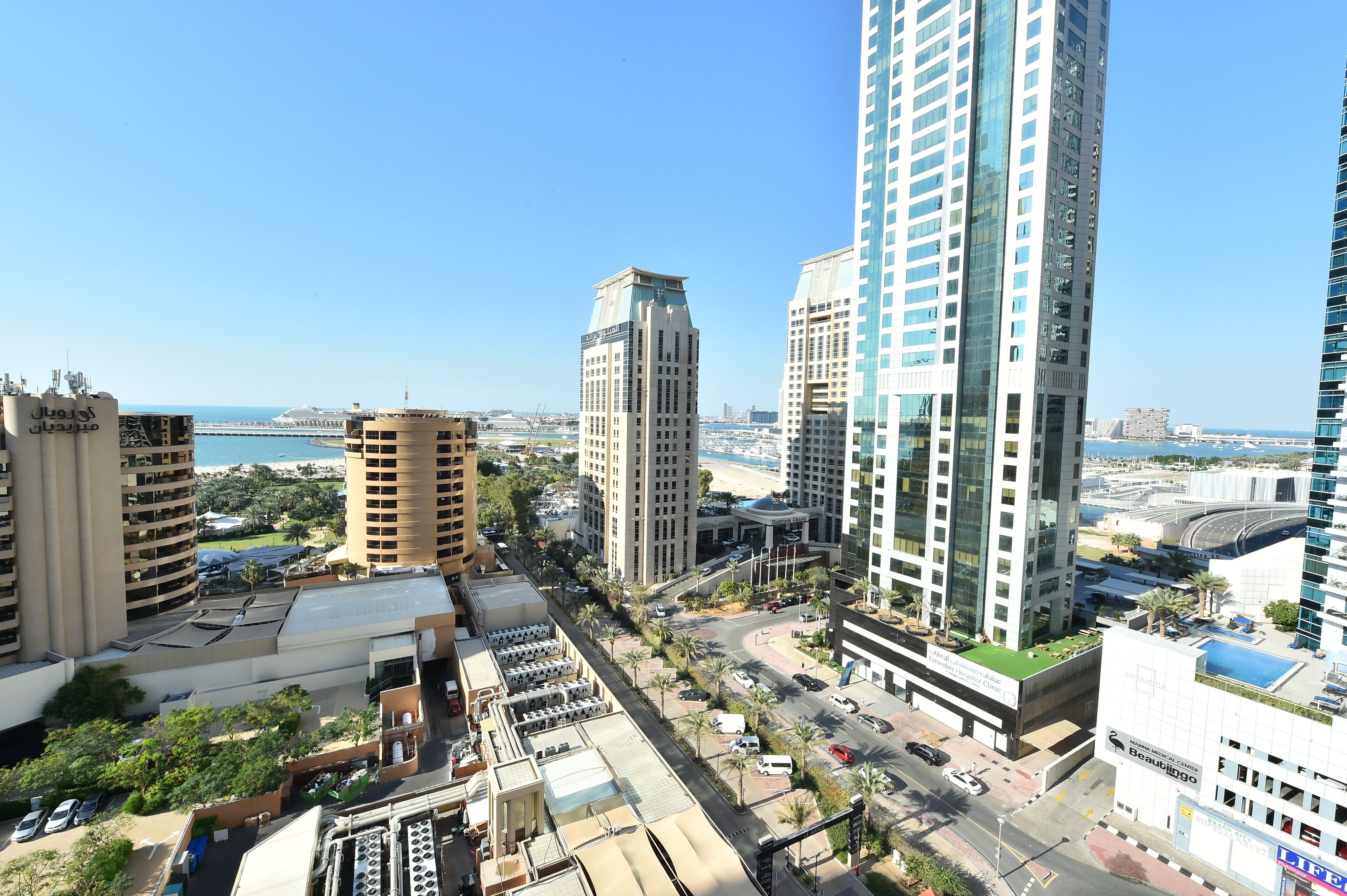 A high-rise urban area with modern buildings, a clear sky, and a view of the sea.