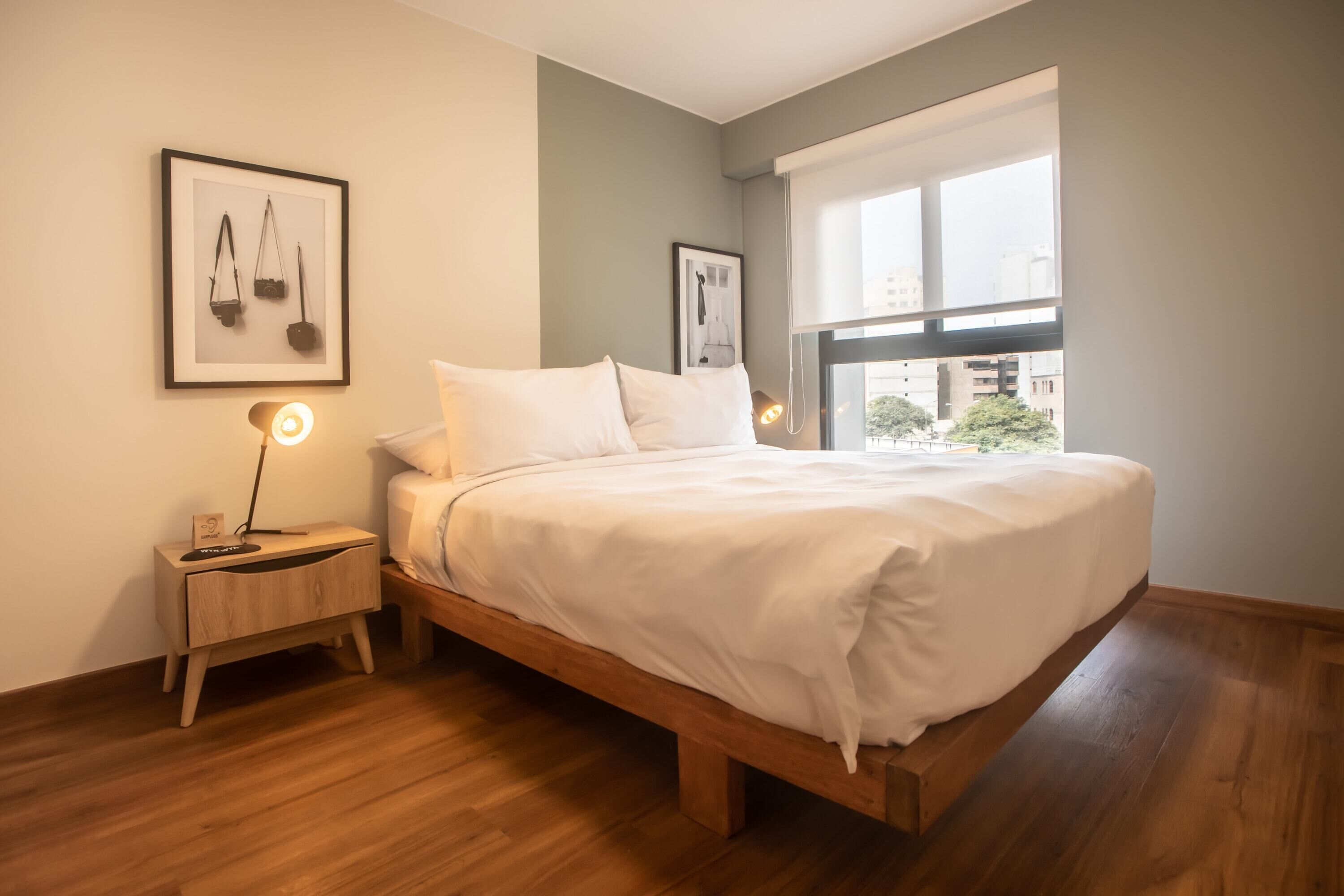 Una camera da letto con un letto di legno, un comodino con una lampada e quadri appesi al muro.
