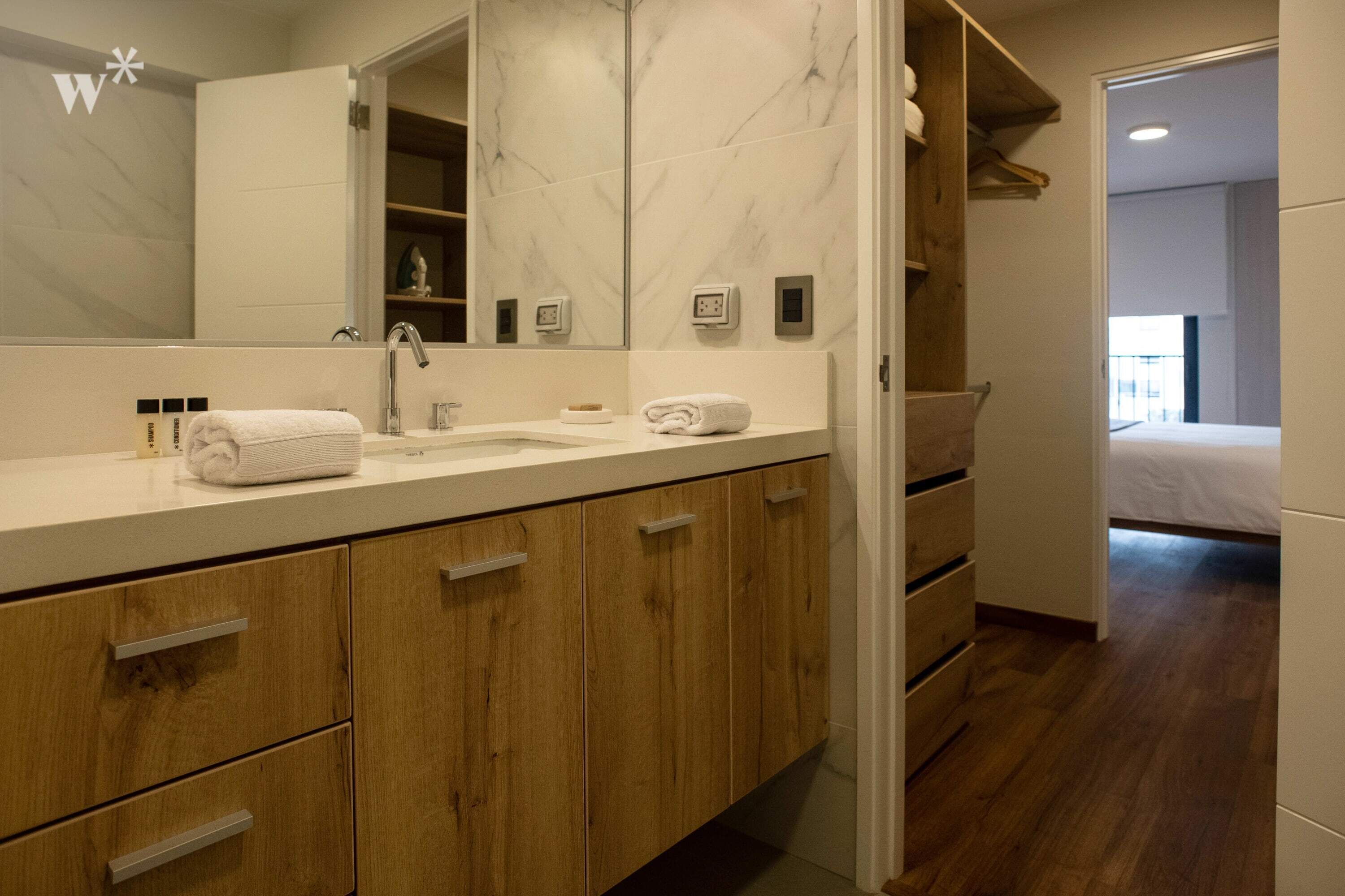 A modern bathroom with a large mirror, wooden cabinets, and a white countertop.