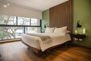 A modern bedroom with a large bed, a view of trees through a window, a wooden floor, and a green accent wall. - Wynwood Alcanfores in Miraflores (Lima)