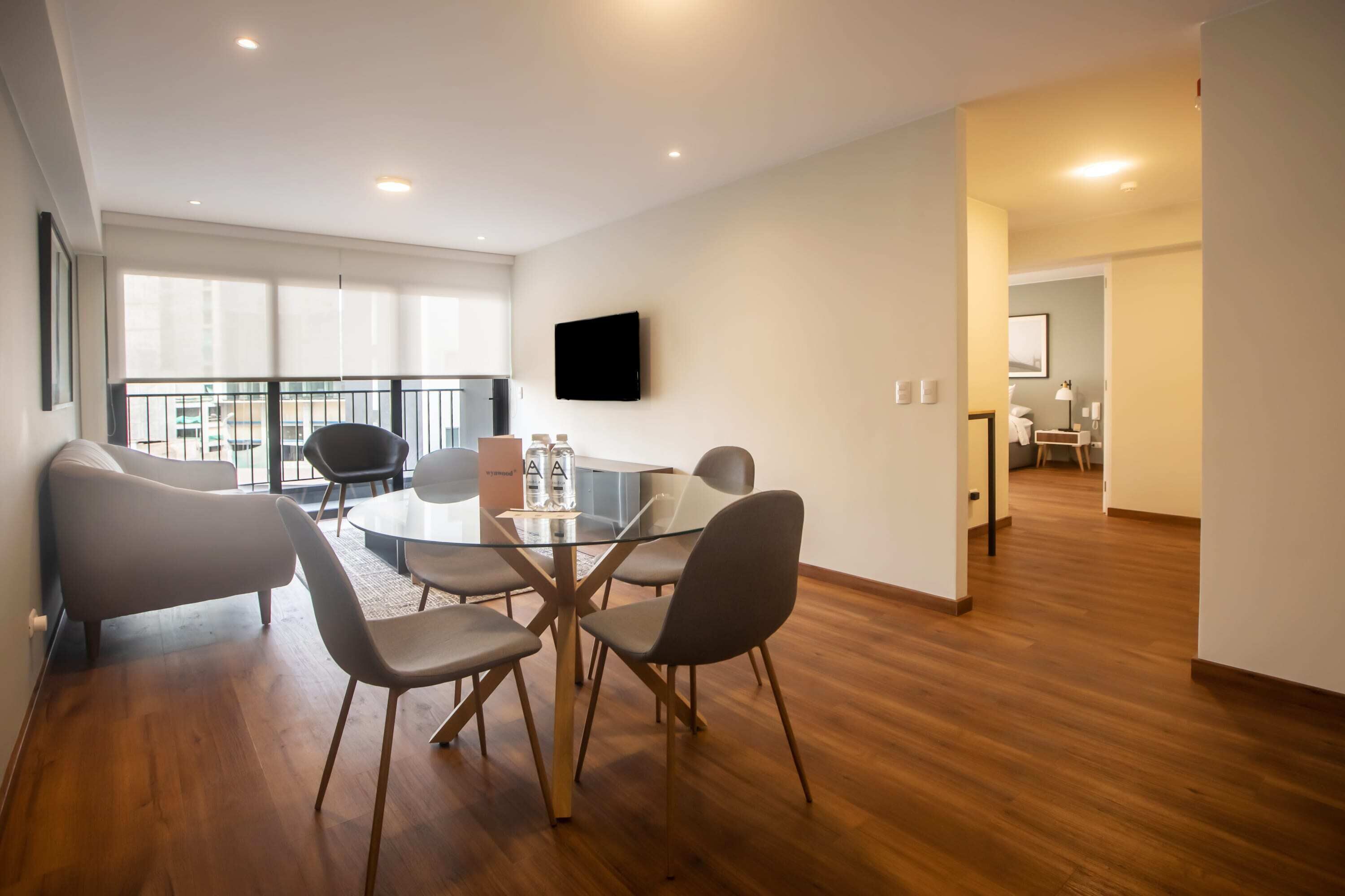 Un moderno comedor con una mesa de vidrio, cuatro sillas y un televisor de pantalla plana en la pared.