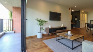A modern living room with a flat-screen TV, a wooden coffee table, a potted plant, and a brick wall.