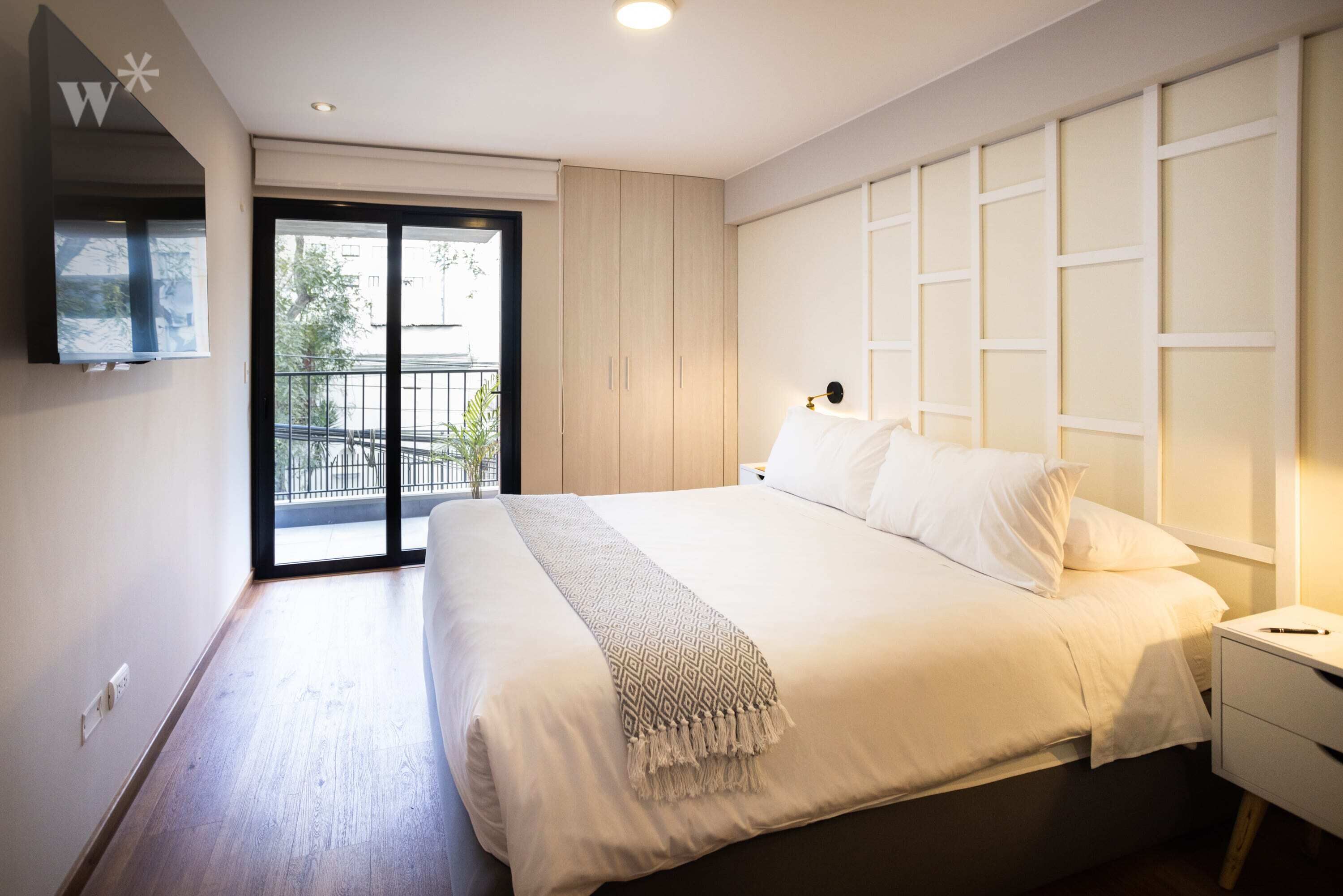Une chambre dotée d’un grand lit, d’un téléviseur fixé au mur et d’une porte-fenêtre coulissante donnant sur un balcon extérieur.