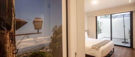 A bedroom with a bed, a view through a glass door, and a balcony with a floor lamp.