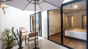 A modern hotel room with a large bed, a wooden bench, and potted plants.