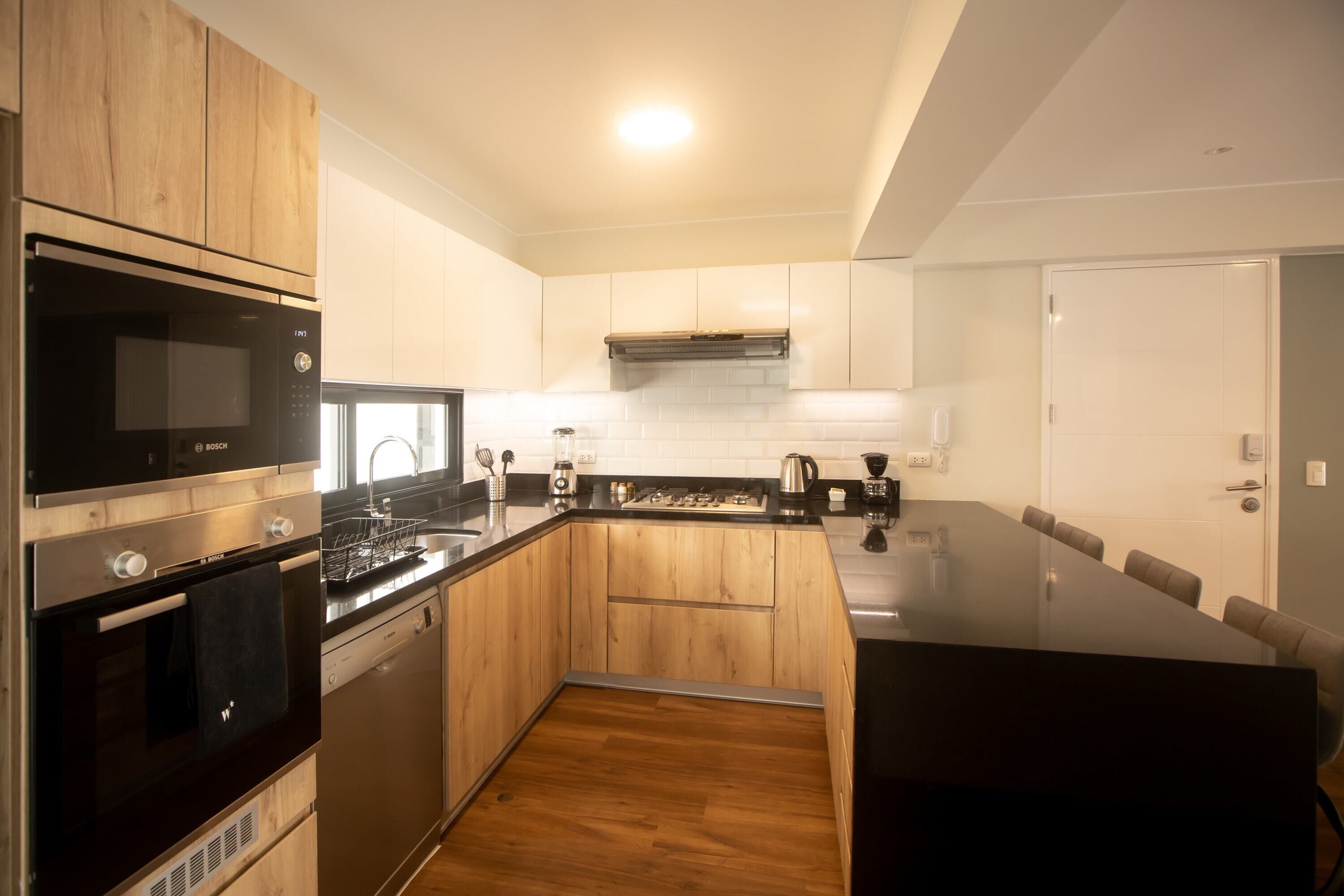 A modern kitchen with wooden cabinets, a Bosch microwave, a dishwasher, and a large island with seating.