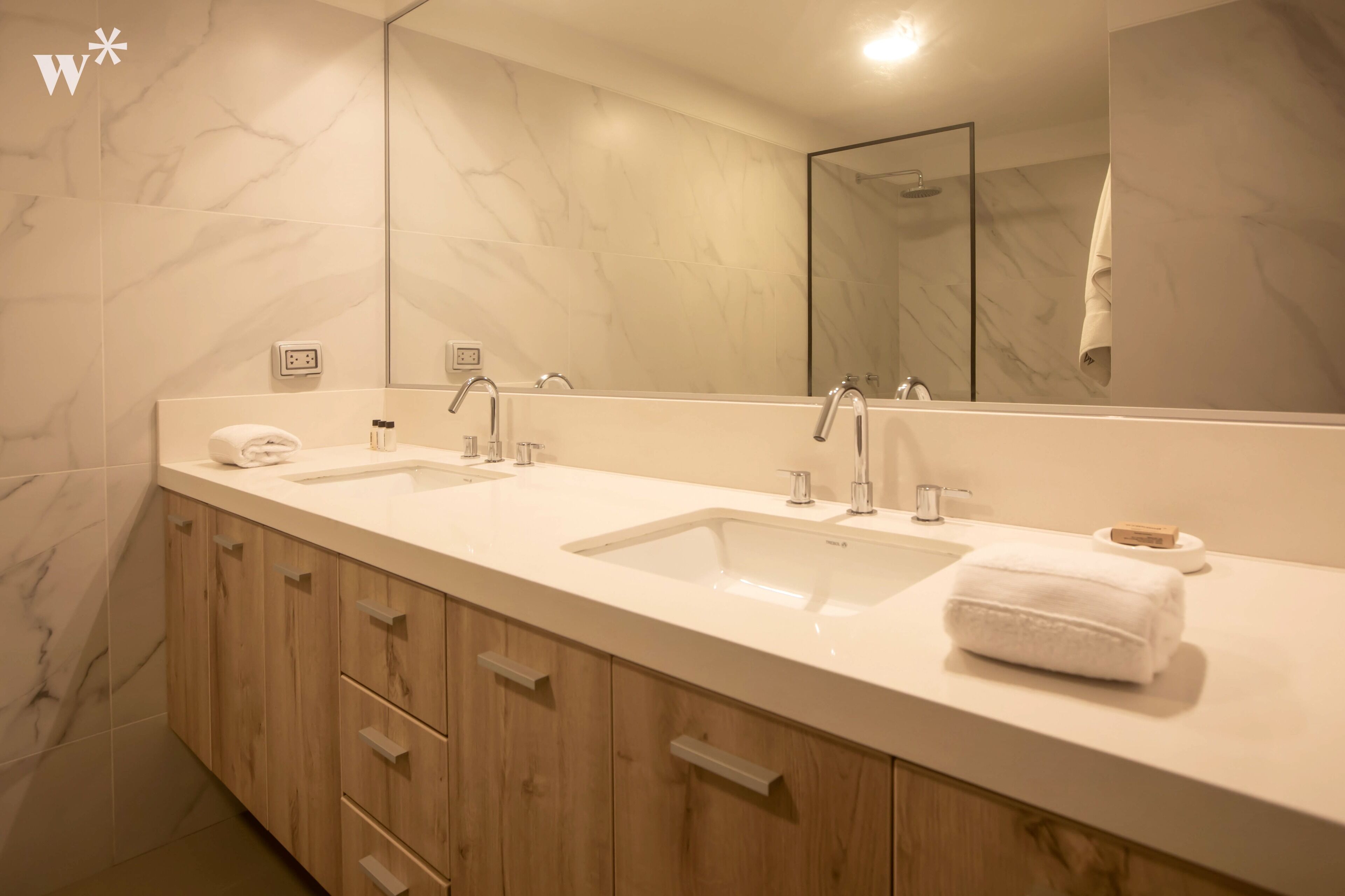 A modern bathroom with two sinks, a large mirror, and wooden cabinets.
