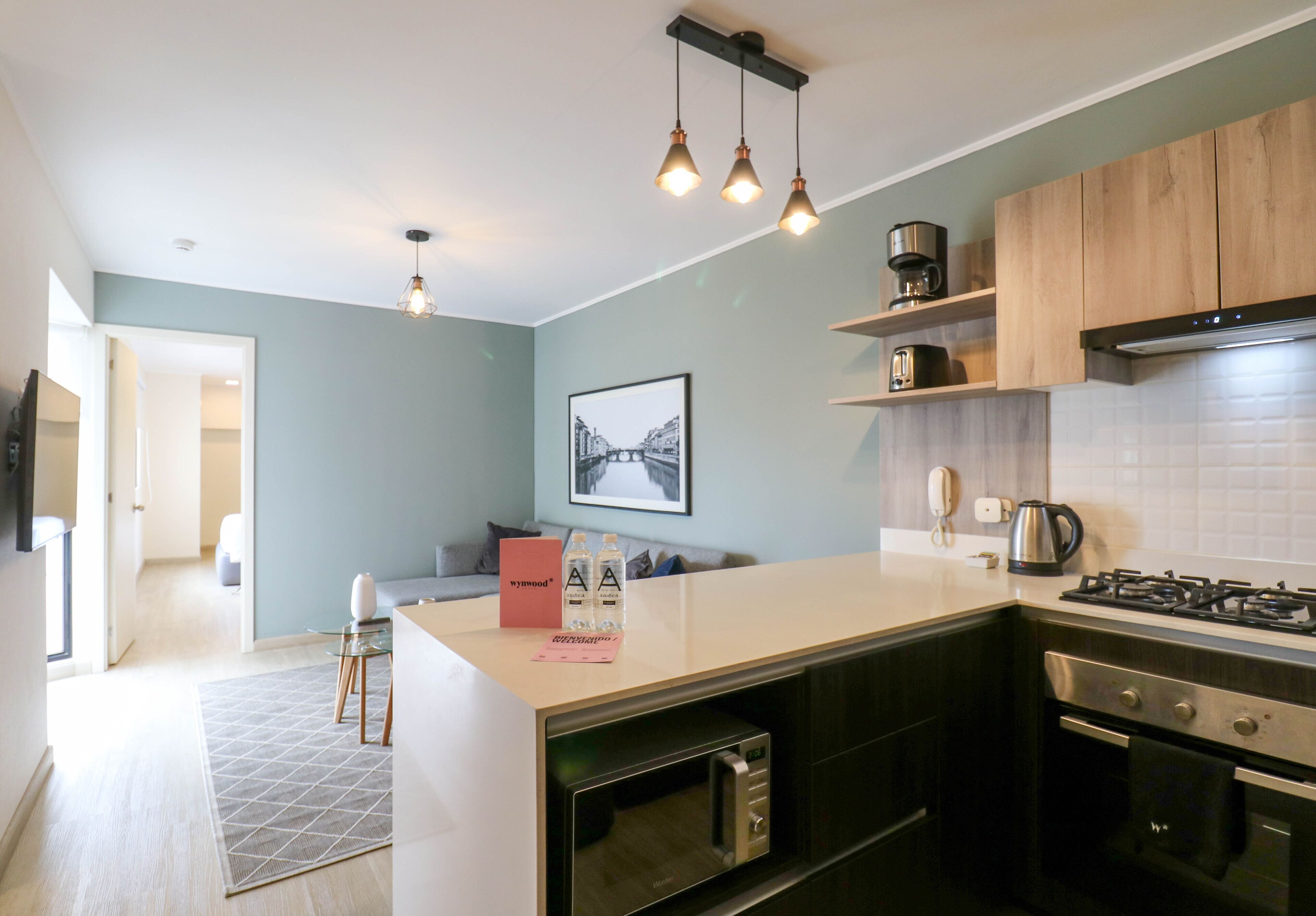 Een moderne keuken met een centraal eiland, een ingebouwde oven en roestvrijstalen apparatuur. Er is een zithoek met een bank en een salontafel.
