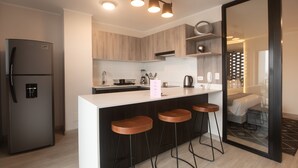 A modern kitchen with a built-in refrigerator, wooden cabinets, a white countertop, and three bar stools. - Wynwood El Sol Este in Barranco (Lima)