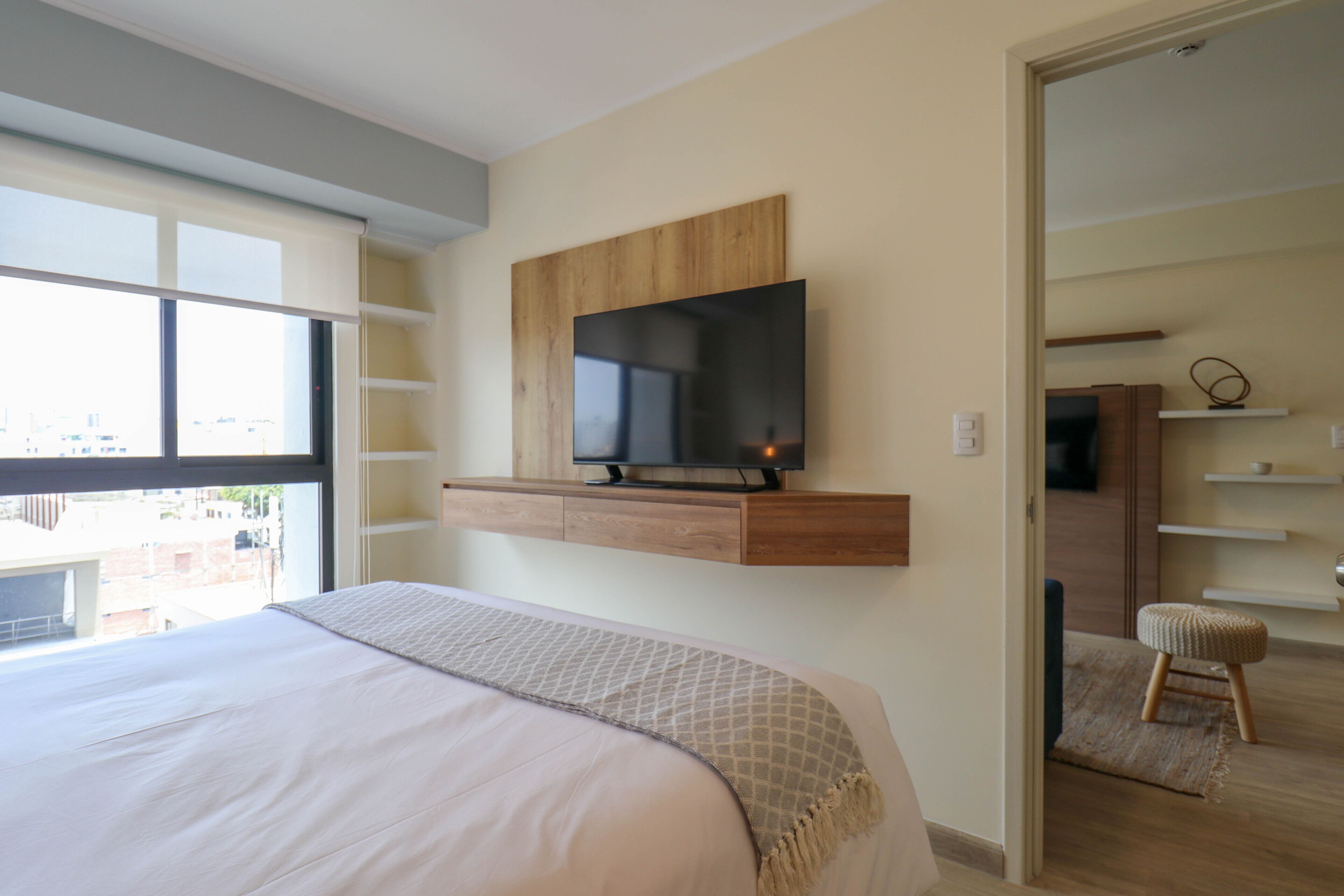 Une chambre à coucher avec un lit, un téléviseur fixé au mur, des étagères intégrées et une vue par la fenêtre.