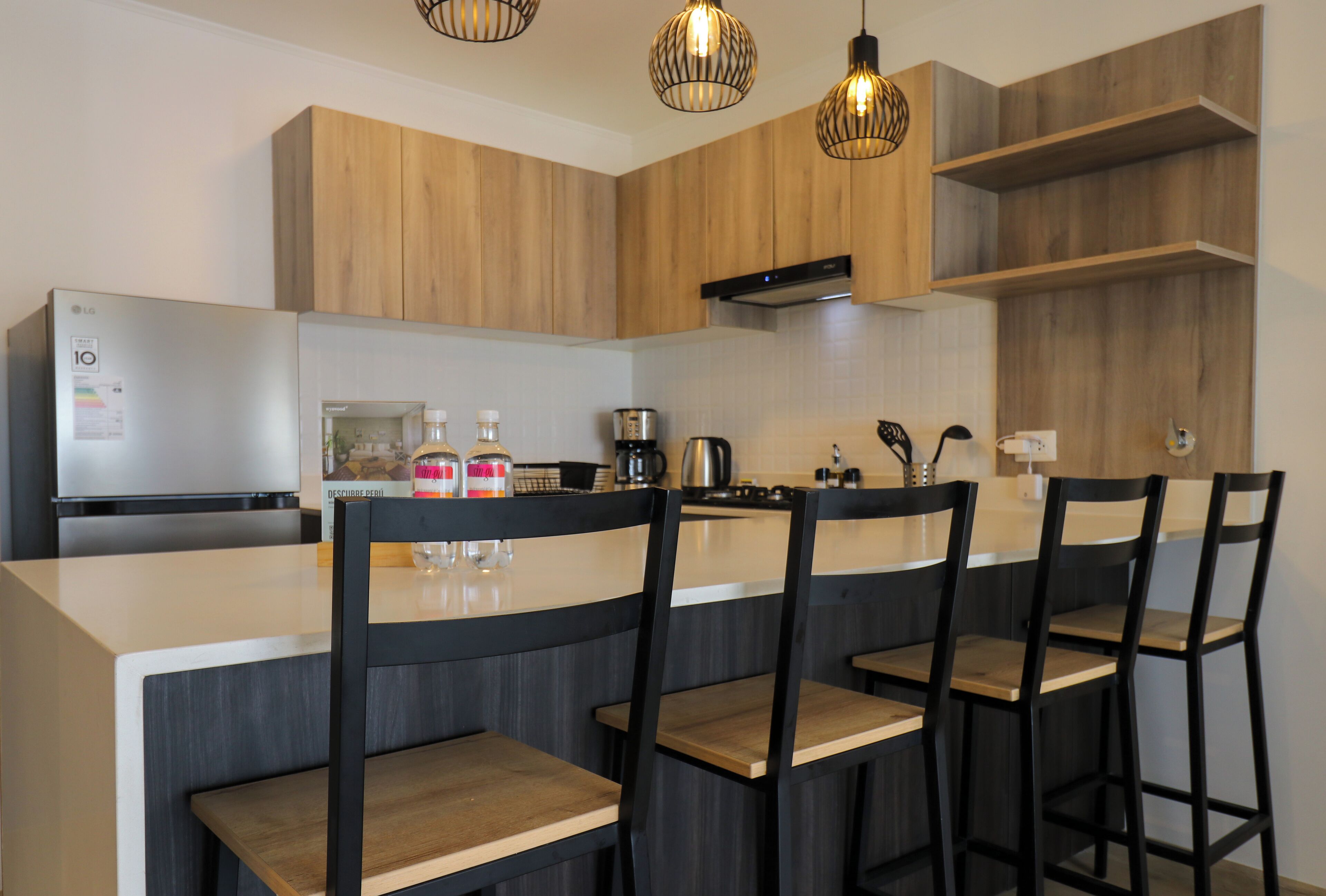 Een moderne keuken met houten kasten, een roestvrijstalen koelkast, een koffiezetapparaat en barstoelen.