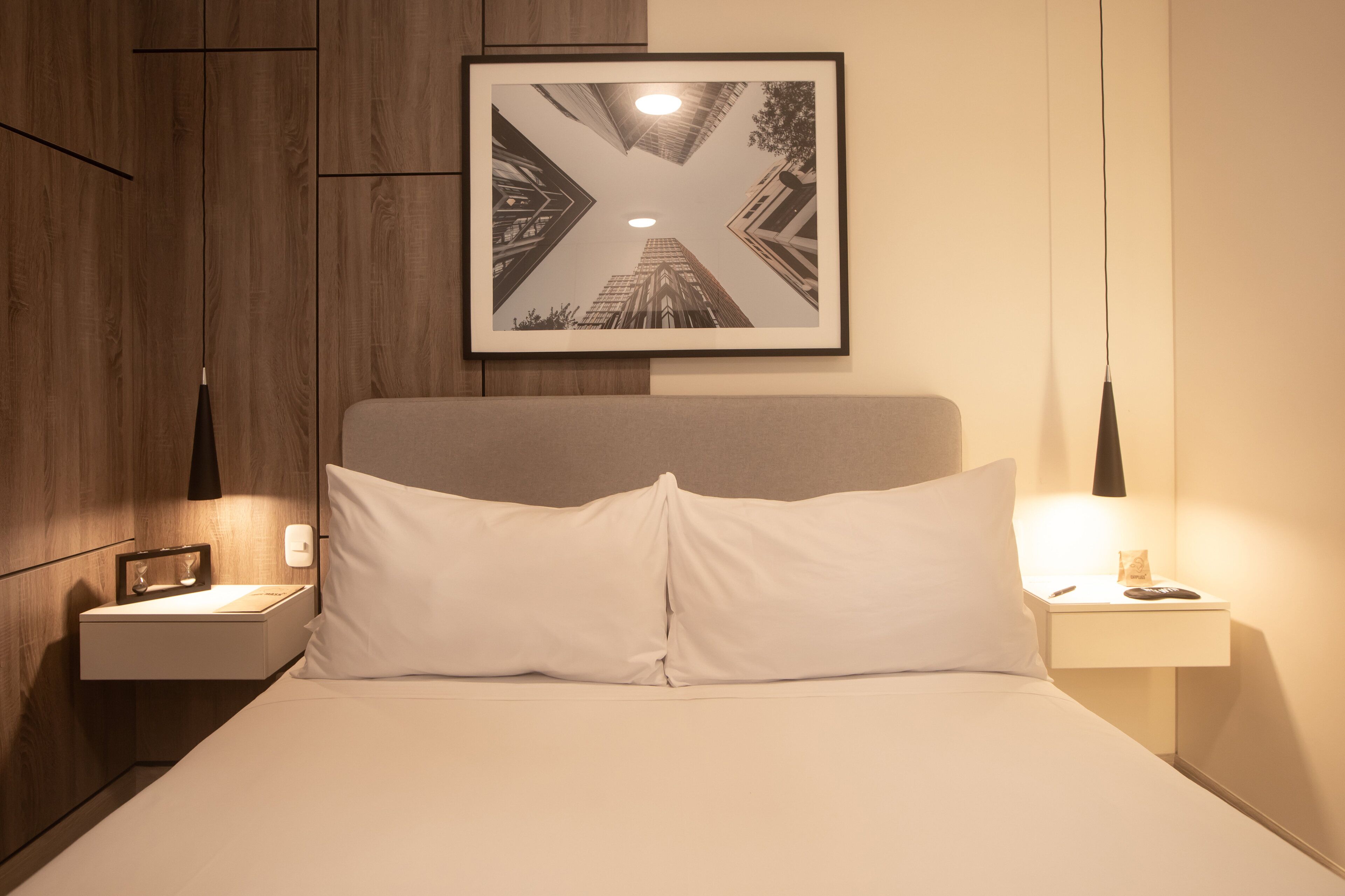 A neatly made bed with white bedding, a framed picture above it, and a bedside table with a lamp.