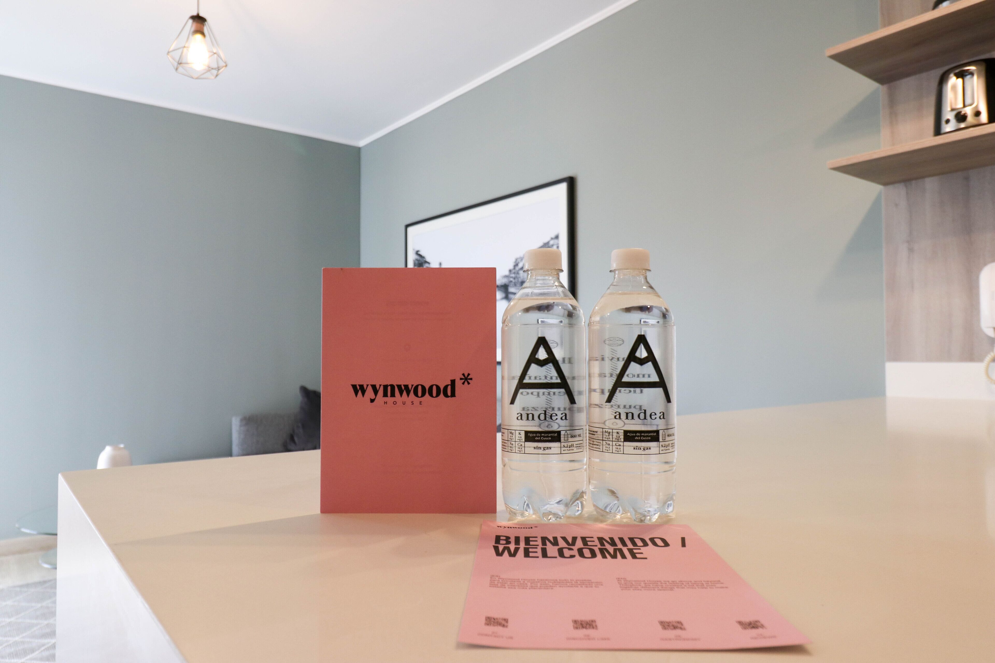 Un mostrador de recepción con un tapete de bienvenida, dos botellas de agua y una caja roja con la etiqueta 'wynwood*'.